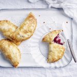 Er liggen 4 appelflappen klaargemaakt op een wit plateautje. Eén appelflap is opengesneden, door de combinatie te maken met blauwe bessen heeft de vulling mooi met appels een mooie rode kleur.