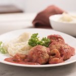 Eén portie balletjes in tomatensaus met puree, komt eraan. Hij staat klaar op een houten tafel, klaar om op te eten.