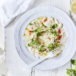 Ceviche van wijting met kleine stukjes koolrabi en appel er bovenop. Hij is geserveerd op een wit bord waardoor de groentjes nog extra opvallen. Er ligt verse munt langs en een witte servette. 