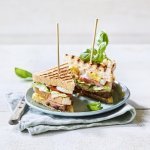 Goedgevulde club sandwich met lamsvlees en rauwkost. Gepresenteerd op een bord met middenin een prikker, klaar om op te eten. 