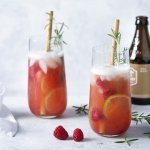 2 cocktails staan uitgeschonken in grote glazen. Deze cocktail op basis van bier en gin werd afgewerkt met frambozen en rozemarijn.