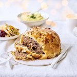 Rond gehaktbrood omhuld met bladerdeeg waarop sterren in bladerdeeg zijn teogevoegd. In het beeld liggen ook het gebraiseerd witloof met veenbessencompote en de puree. Kerstlampjes zien je flou in de foto.