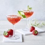 Cocktail time! Wij serveren een frozen daiquiri met verse aardbeien en basilicum. We presenteren hem in een wijnglaasje met suikerrandje, schijfje limoen en basilicumblaadje. Er liggen enkele aardbeien langs samen met witte bloemetjes. Schol! 