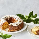 Een tulband cake met groenten als bijgerecht bij je middagmaal, dat is pas een feestmaaltijd! Wij maakten eentje met pompoen, rode biet, Belgische kaas en kastanjes. Hij staat op een witte houten tafel op een wit groot bord, de cake is afgewerkt met een garnering van zure room.