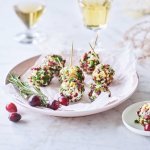 Kruidige kaasballetjes liggen op een licht roos bordje. Op de achtergrond staan 2 glaasjes aperitief met enkele veenbessen ter versiering. 