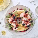 Een echte Kerstkrans om op te eten. De krans is gemaakt van een Turks brood die belegd werd met verschillende vleesjes, fruit en rozemarijn. Hij staat op de feesttafel en enkele zilveren sterren liggen er langs vergezeld met enkele aperitiefjes. 