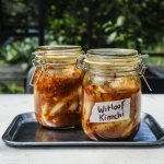 Er staan twee weckpotten op een inoxe plateau gevuld met kimchi. Hij is roodkleurig door de toevoeging van chilisaus. 