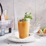 Een gazpacho van paprika geserveerd in een groot glas zorgt intens voor een feestlook. Deze koude soep werd gepimpt met stukjes komkommer en tomaat, als afwerking nog enkele blaadjes koriander en zonnebloempitten bovenop. 