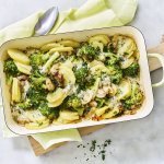 Een ovenschotel van aardappel, broccoli, champignons en blauwe kaas staat op het midden van het marmere aanrecht op een houten snijplank. Verse kruiden zorgen voor een extra groene touch!