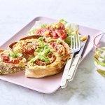 Een klaargemaakte quiche ligt op een roze en rechthoekig bord klaar om te eten. De quichebodem bestaat uit een wrap met hierin het quichebeslag en de groenten. 