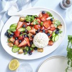 Er staat een grote schaal op tafel boordevol zomerse toppers. Denk maar aan tomaatjes, aardbeien, bosbessen, komkommers en burrata. Dit geeft echt verfrissing tijdens een zwoele zomerdag. Er ligt een citroentje langs, een glas water en verse kroiander.