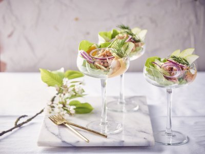 Garnalencocktail met appel en selderij Drie garnalencocktails staan geserveerd op een marmer aanrecht, in mooie wijnglazen met een brede opening bovenaan. Er liggen gouden vorkjes naast om het feestgehalte een extra boost te geven.