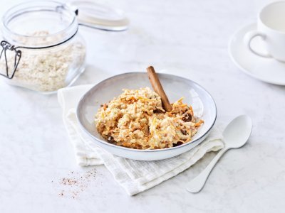 Overnight oats met geraspte wortel Een heerlijk ontbijtje dat smaakt naar worteltaart, dat kan je niet weerstaan! De overnight oats is geserveerd in een licht grijs diep bord, witte lepel langs en een kop verse koffie. Helemaal klaar om wakker te worden.