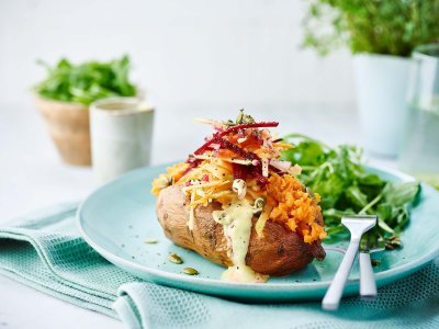 Gepofte zoete aardappel met wortelen, radijsjes, rode biet en appel gepresenteerd op een blauw bord met een rucola slaatje als bijgerecht.