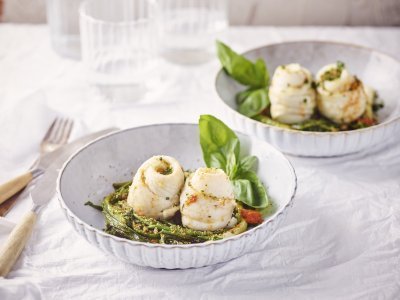 Schartongrolletjes met tomatenboter, zeekraal, lente-uitjes en crumble van ansjovis en peterselie Twee bordjes staan op tafel, het zijn diepe borden in een lichtblauwe/grijze kleur. Ze zijn gevuld met de lente-uitjes en zeekraal op de bodem in een nestjesvorm. Hier bovenop liggen de schartongrolletjes. Het gerechtje is afgewerkt met de tomatenboter en crumble van ansjovis en peterselie.