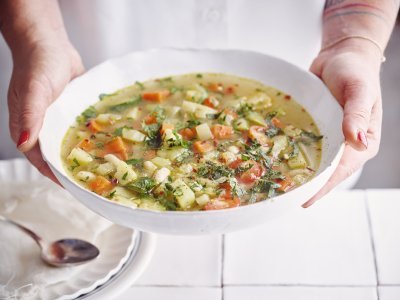 Vegetarische minestrone Een vegetarische minestrone met venkel, witte bonen, aardappel en verse kruiden geserveerd in een diep wit soepbord. Een vrouw met mooi rood gelakte nagels draagt het bord.