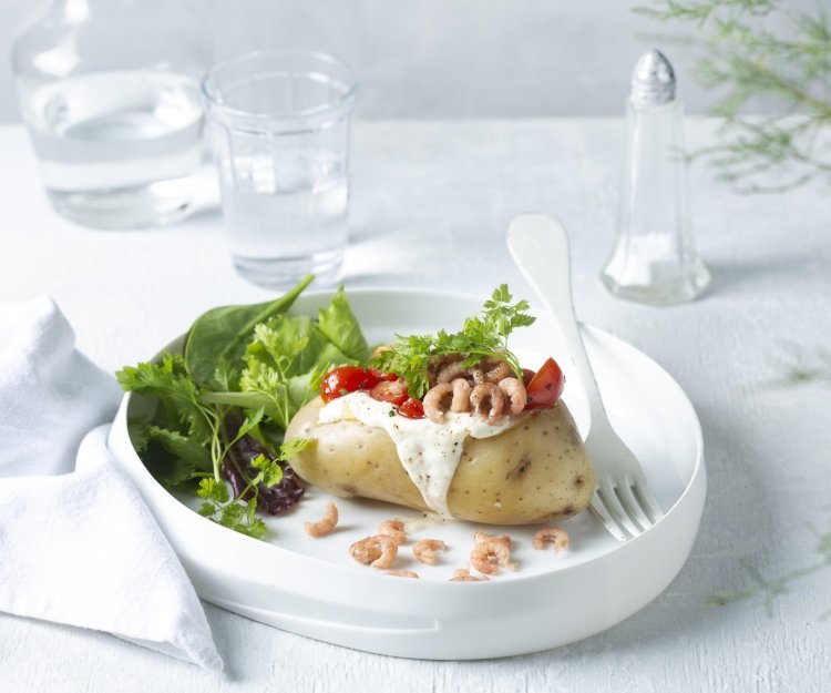 Aardappel in de schil met zure room, garnalen en kerstomaatjes Een gepofte aardappel feestelijk afgewerkt met zure room, garnaaltjes en kerstomaatjes. Het gerechtje is afgewerkt met een groene salade dat instant kleur geeft aan het gerecht.