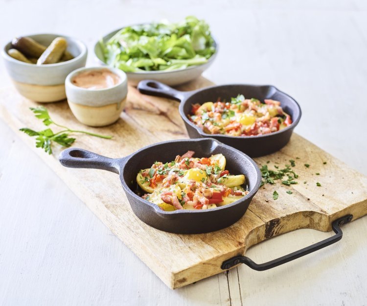 Aardappelplakjes met spek, paprika en kaas voor de gourmet Twee gourmetpannetjes staan te sieren op een houten snijplank. Als bijgerechtjes hebben we een groene salade, opgelegde augurkjes en een cocktailsausje.