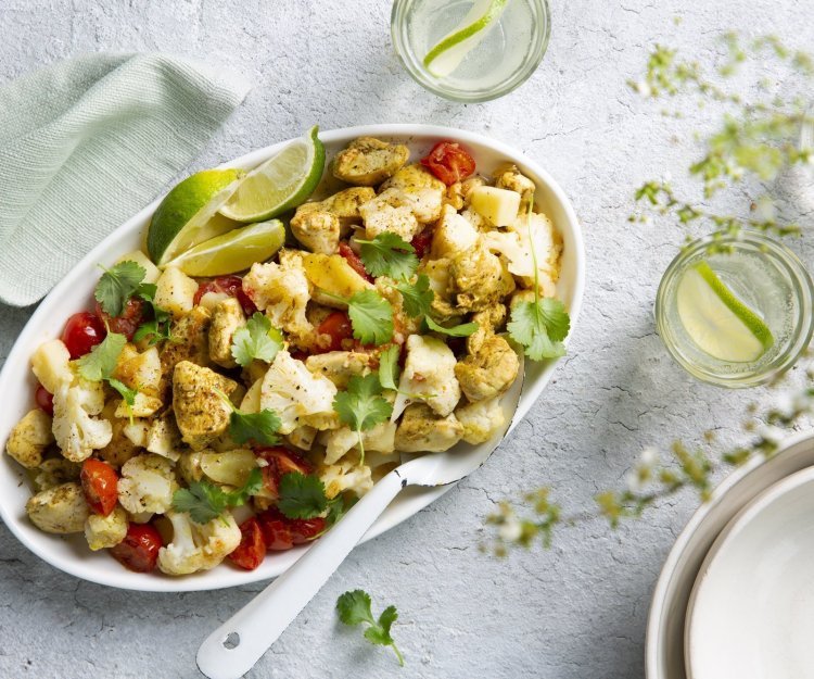 Aloo gobi is een Indiase curry van aardappel en bloemkool. Wij deden er nog stukjes kip bij. Deze rijkgevulde schotel van groenten en kruiden staat op tafel met een grote witte lepel bij. Voor de afwerking werd deze schotel gepresenteerd met korianderblaadjes en limoenpartjes. 