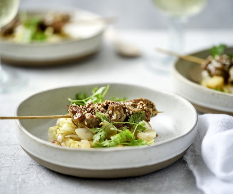 Er staan verschillende aperetiefbordjes op tafel met een schepje gestoofd witloof en appel. Hierop ligt een klein brochette van rundvlees en afgewerkt met kervel. 