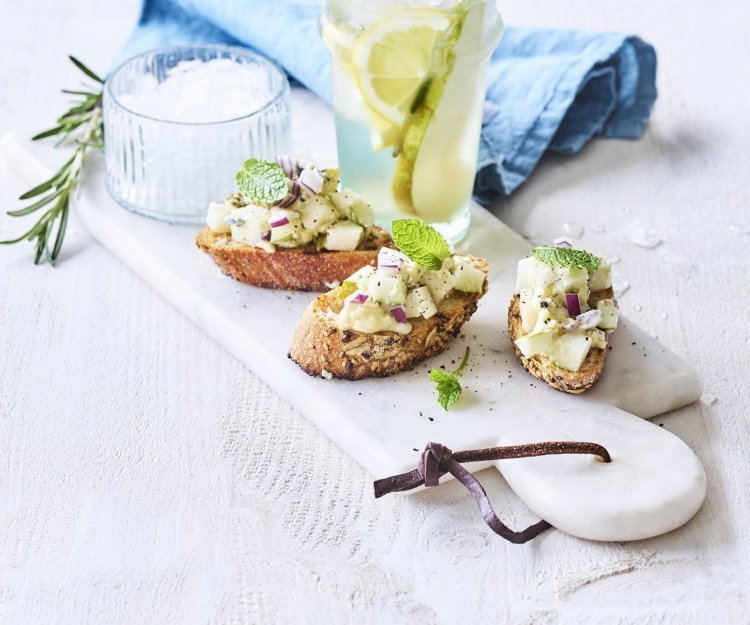 Bruschetta met perensalsa en blauwe schimmelkaas liggen op een marmer schaaltje samen met een homemade rozemarijnlimonade met peer. 