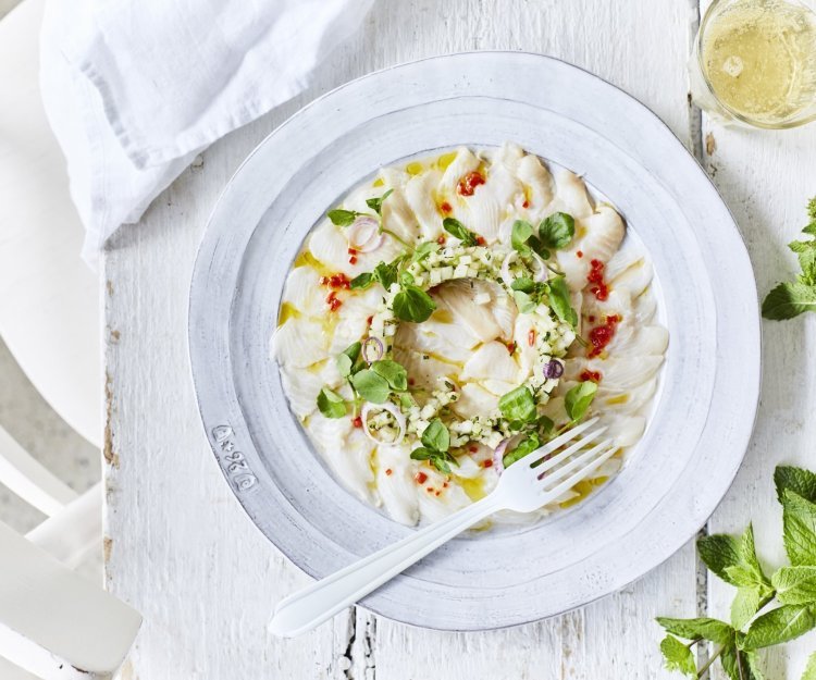 Ceviche van wijting, koolrabi en appel Ceviche van wijting met kleine stukjes koolrabi en appel er bovenop. Hij is geserveerd op een wit bord waardoor de groentjes nog extra opvallen. Er ligt verse munt langs en een witte servette.