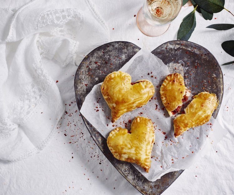 Empanadas gemaakt in hartjesvorm liggen op een bordje te schitteren. Met dit hapje scoor je sowieso bij je geliefde. 