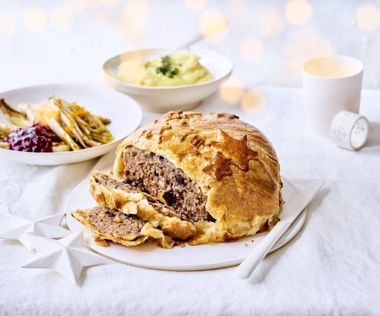 Rond gehaktbrood omhuld met bladerdeeg waarop sterren in bladerdeeg zijn teogevoegd. In het beeld liggen ook het gebraiseerd witloof met veenbessencompote en de puree. Kerstlampjes zien je flou in de foto.