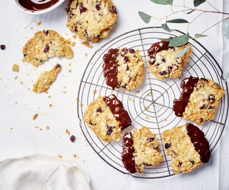 Krokante amandelkoekjes liggen af te koelen op een taartrooster. Ze zijn mooi goudgeel gebakken en zijn 1/4 gedipt in gesmolten chocolade.