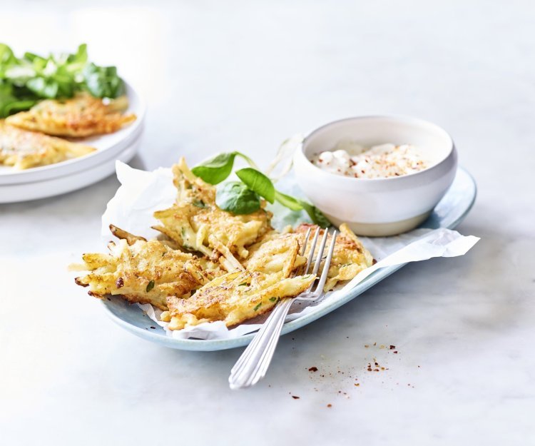 Fritters van aardappelen en Belgische kaas Meerdere fritters liggen op een licht blauw bordje vergezeld van een blaadje veldsla en het dipsausje op basis van yoghurt en specerijen.
