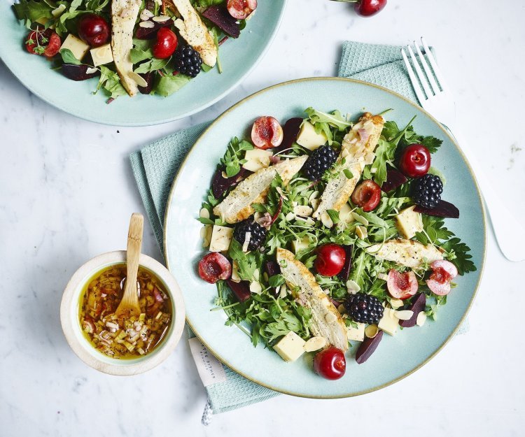 Fruitige salade met rode biet en gegrilde kip Een gemengde salade met sla, kersen, bramen en gekookte kipfilet gedresseerd op een lichtblauw bord. De dressing is er naast gezet in een keramieke potje met houten lepeltje in, de dressing bestaat uit sjalot, rode wijazijn, olijfolie en peper en zout.