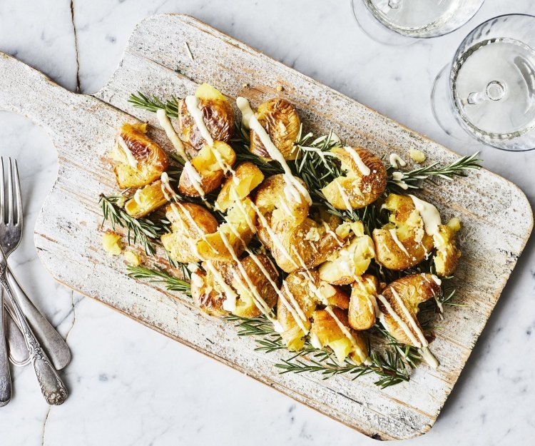 Gecrushte aardappelen met picklessausje Eens een patatje in een feestjas op tafel? Serveer deze ovenaardappeltjes en ontvang veel "mmmmm-lekker complimentjes". Deze gecrushte aardappeltjes zijn geserveerd op een houten plank met een heerlijk picklessausje.