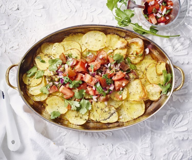 Gegrilde aardappelen met tomatensalsa Aardappelschijfjes liggen gestapeld in een kopere ovenschaal. Hierop is de rode tomatensalsa geschept dat een mooi beeld geven tov het goudgele van de gegrilde patatjes. Her gerechtje is afgewerkt met korianderblaadjes.