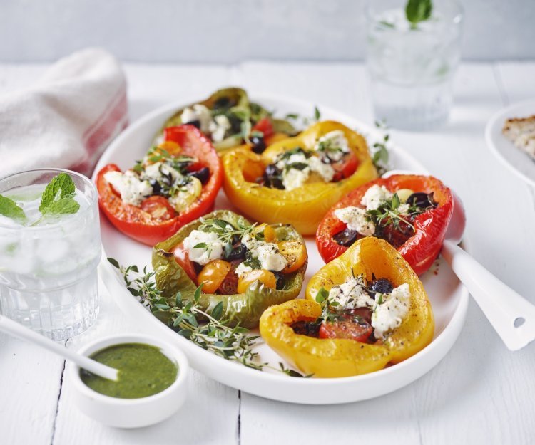 Gegrilde paprika’s gevuld met tomaat en Belgische ricotta Zes halve paprika's liggen op een grote witte schaal. De paprika's zijn opgevuld met kerstomaatjes, olijven en ricottakaas.