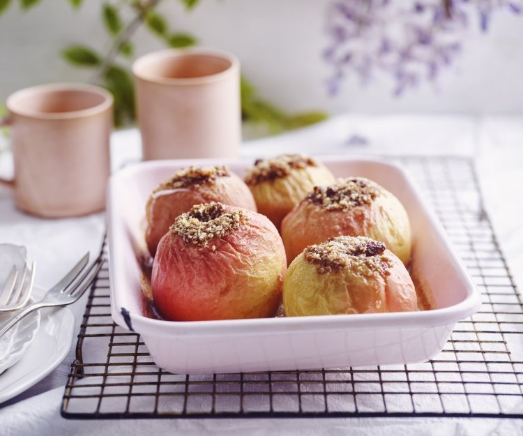 Gevulde appel met speculaas, rozijnen en walnoten Gevulde appels in een licht roze ovenschaal. Achteraan staan twee roze kopjes, klaar om aan het ontbijt te beginnen.