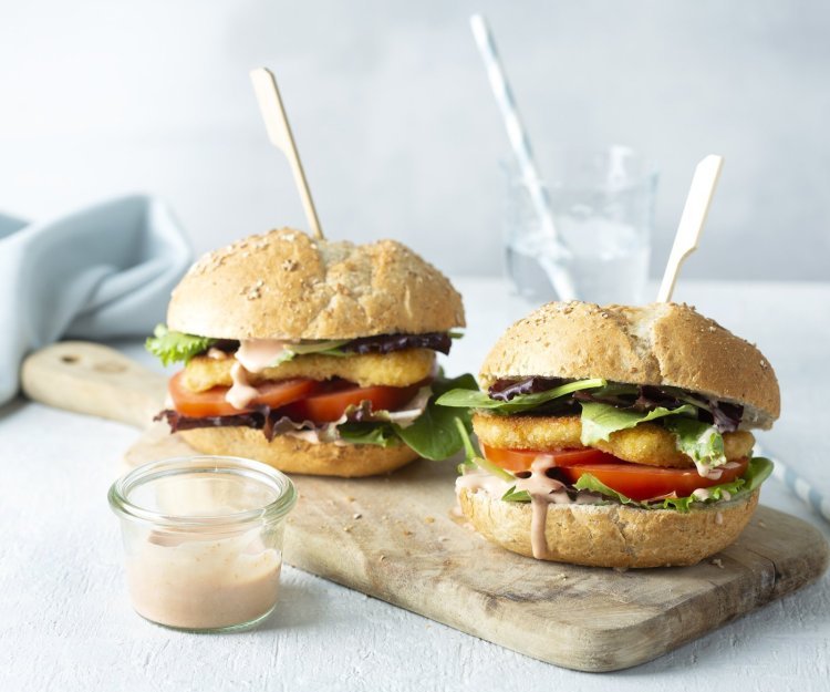 Een heerlijke hamburger die niemand koud laat. We maakten hem extra crunchy door de kaas te paneren alvorens hem te bakken. De twee hamburgers liggen op een houten snijplank met een prikker middendoor. 