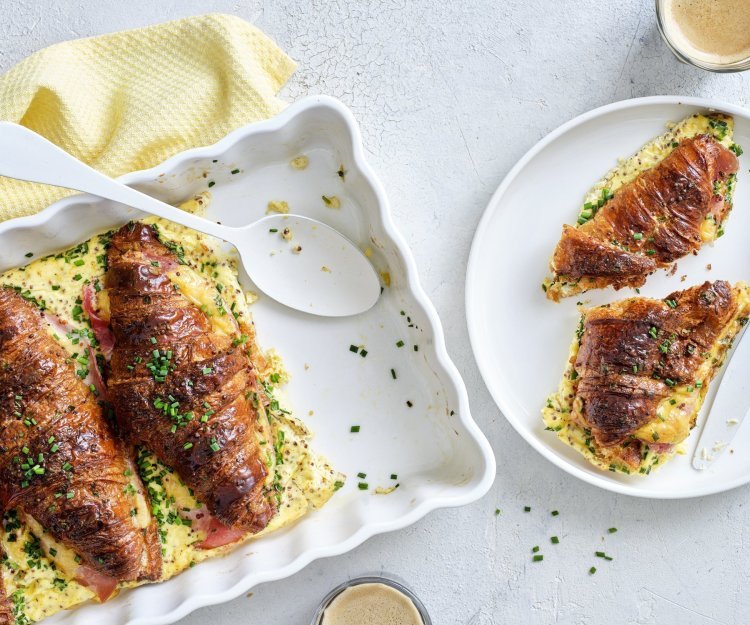 Er staat een witte ovenschotel op tafel gevuld met croissants. Ze zijn doormidden gesneden, bestrijkt met mosterd en belegd met ham en kaas. Daarna is een beslag toegevoegd en werden ze 10 minuten in de oven geplaatst. Om vingers en duimen van af te likken, al zeg ik het zelf.