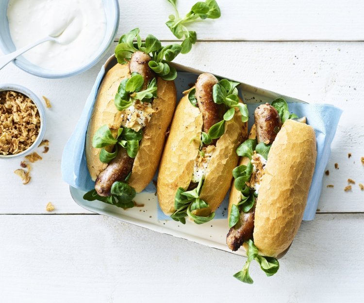 Hotdog met varkensworst 3 hotdogs liggen klaar om gegeten te worden. Ze zijn vergezeld met groene groentjes en een sausje.