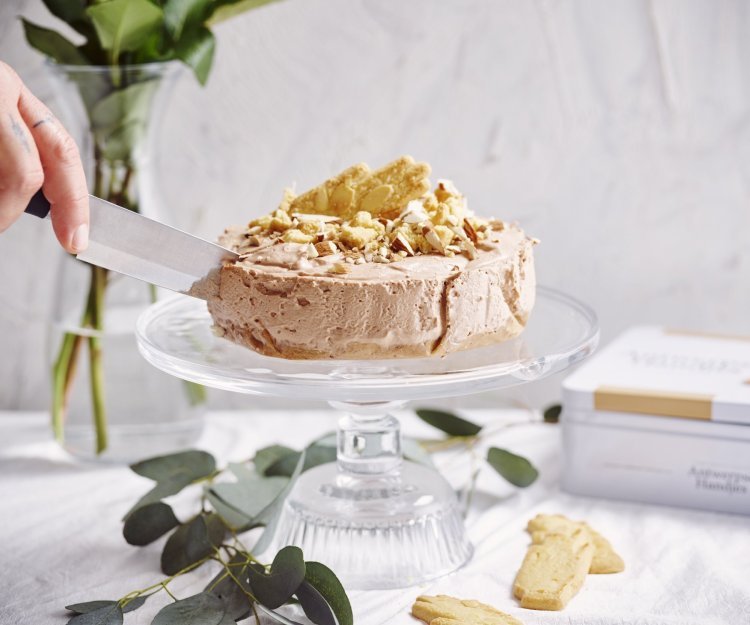 Kaastaart met chocolade en Antwerpse handjes Een heerlijke no-bake taart die niemand koud laat. De cheesecake staat op een hoge taartenschaal en wordt aangesneden. De kaastaart is er eentje met chocolade, Antwerpse handjes en Maltesers. Heerlijk lekker met andere woorden.