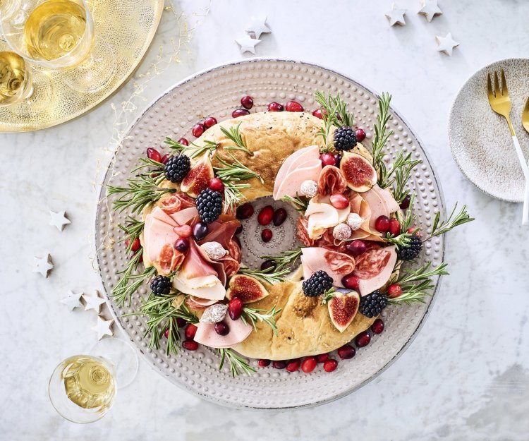 Een echte Kerstkrans om op te eten. De krans is gemaakt van een Turks brood die belegd werd met verschillende vleesjes, fruit en rozemarijn. Hij staat op de feesttafel en enkele zilveren sterren liggen er langs vergezeld met enkele aperitiefjes. 