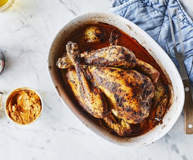 Een heerlijk gegrilde kip uit de oven ligt in een ovenshaal. Ze is heerlijk krokant gebakken en lekker sappig door de homemade kruidenboter. Ze staat op het marmere aanrecht met blauwe nap er langs. 