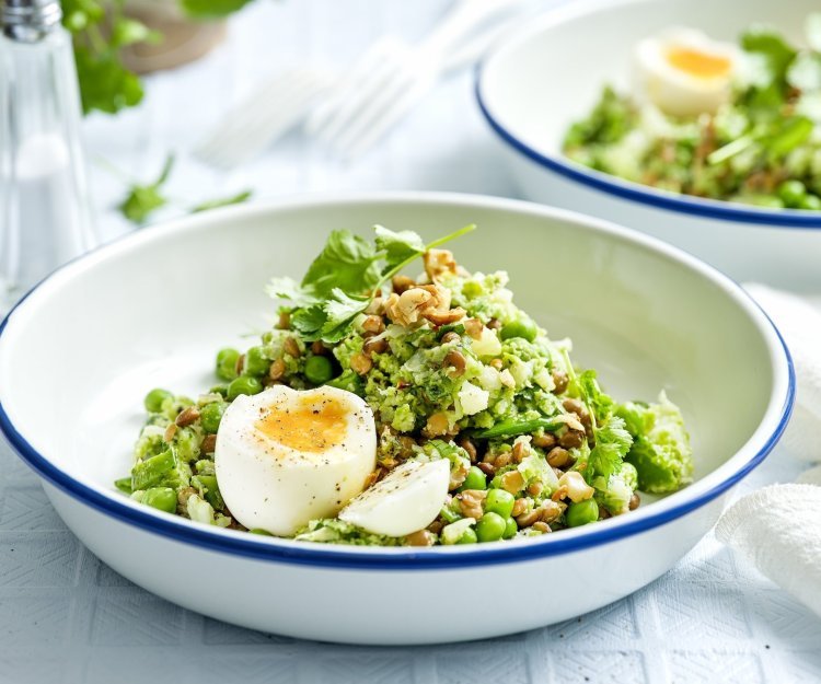Linzensalade met peultjes, bloemkool, erwten en gekookt eitje Een wit emaille bordje met blauwe rand is gevuld met de linzensalade. Het is een salade rijk aan groene groenten. Het gerecht is afgewerkt met een gekookt eitje.