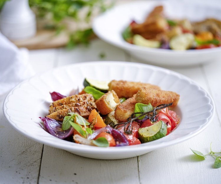 Maaltijdsalade met krokante berloumi Een heerlijk en rijkgevuld slaatje is geserveerd in een diep wit bord. De kleurtjes van de basilicum, tomaten, rode ui en courgette zijn uitgesproken en zien er fantastisch uit. Dit gerecht geeft je een boost.