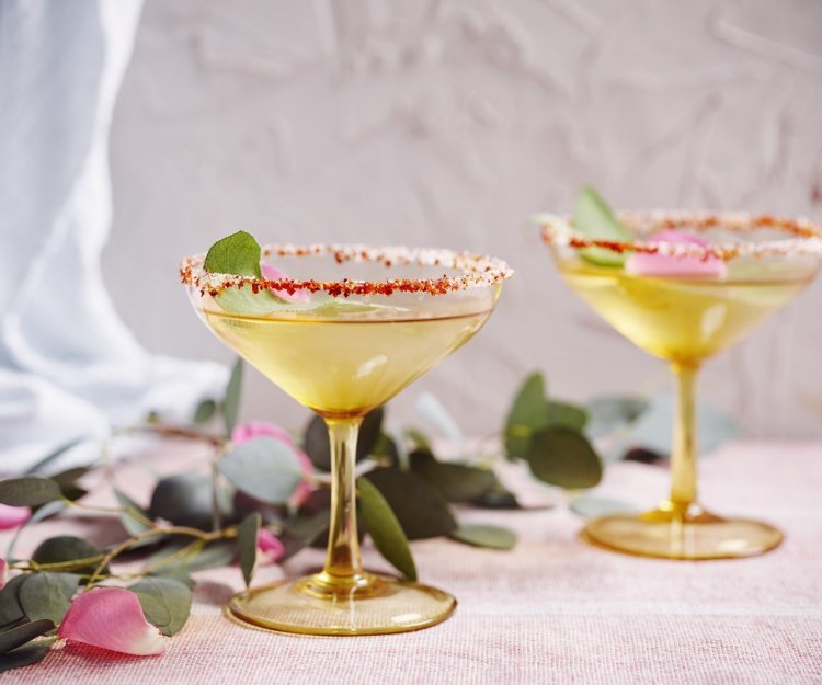 Mocktail van appelsap, vlierbloesemsiroop en salie Twee glaasjes staan klaar om te klinken. De mocktail is geschonken on the rocks en het glaasje is afgewerkt met een kruidig suikerrandje. Ideaal om wat pit in de relatie te brengen.