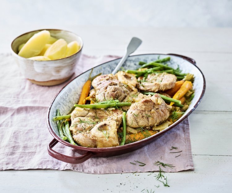 De kalfsschenkels liggen in een ovenschotel met groene boontjes en oranje wortels erbij. Dit zorgt voor een mooie variant op de klassieke ossobuco.