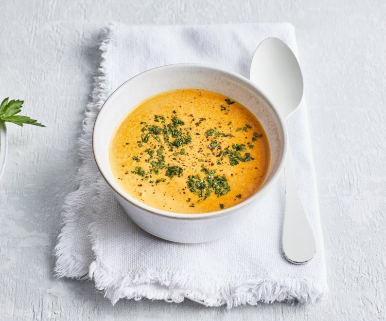 Paprikasaus Deze paprikasaus zit een wit kommetje wat een mooi contrast geeft met de oranje kleur van de saus. Er ligt een witte lepel langs en de saus is afgewerkt met verse groene kruiden.