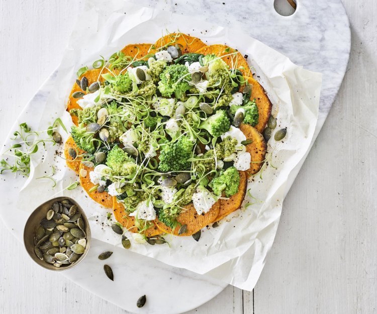 Pizza van zoete aardappel met geitenkaas en groene groenten Klaargemaakt pizza van zoete aardappelschijfjes ligt op een snijplank van marmer. De pizza werd belegd met geitenkaas en groene groenten.