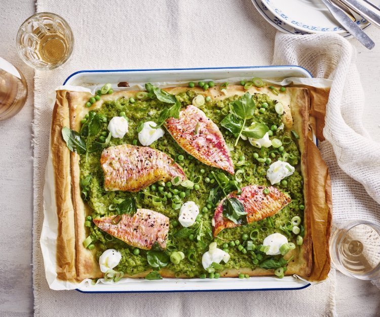 Plaatpizza met erwtenspread, waterkers en zeebarbeel Een plaatpizza staat op het midden van de tafel, klaar om aan te vallen. De plaatpizza kleurt mooi groen door de spread van erwten, hij is afgewerkt met toefjes verse kaas, blaadjes waterkers en de gebakken vis.