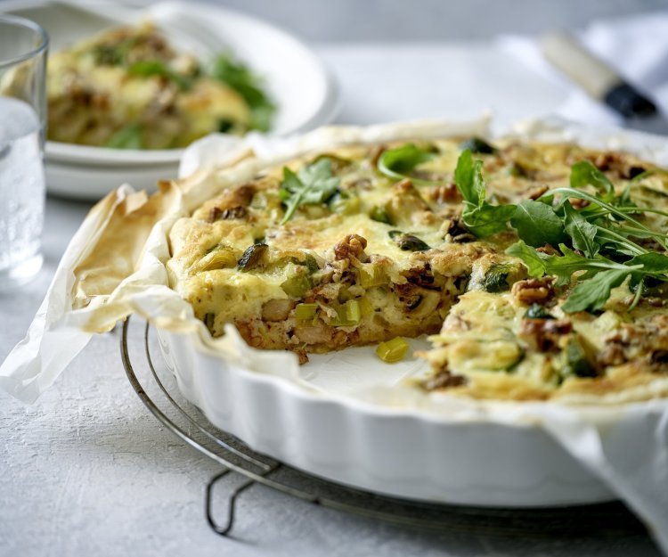 Een heerlijke quiche vers gebakken in een witte porseleinen taartvorm. Hij is gemaakt met spruitjes, champignons en prei. We voegden nog wat walnoten toe voor een extra bite. 