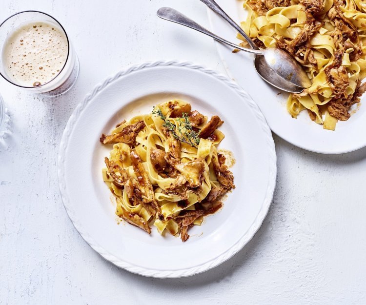 Ragout van konijn met Belgisch bier Op tafel staat een wit bord gevuld met tagliatelle en konijnenragout. Er staat een biertje langs, aangezien de ragout gemaakt is met Belgisch bier.